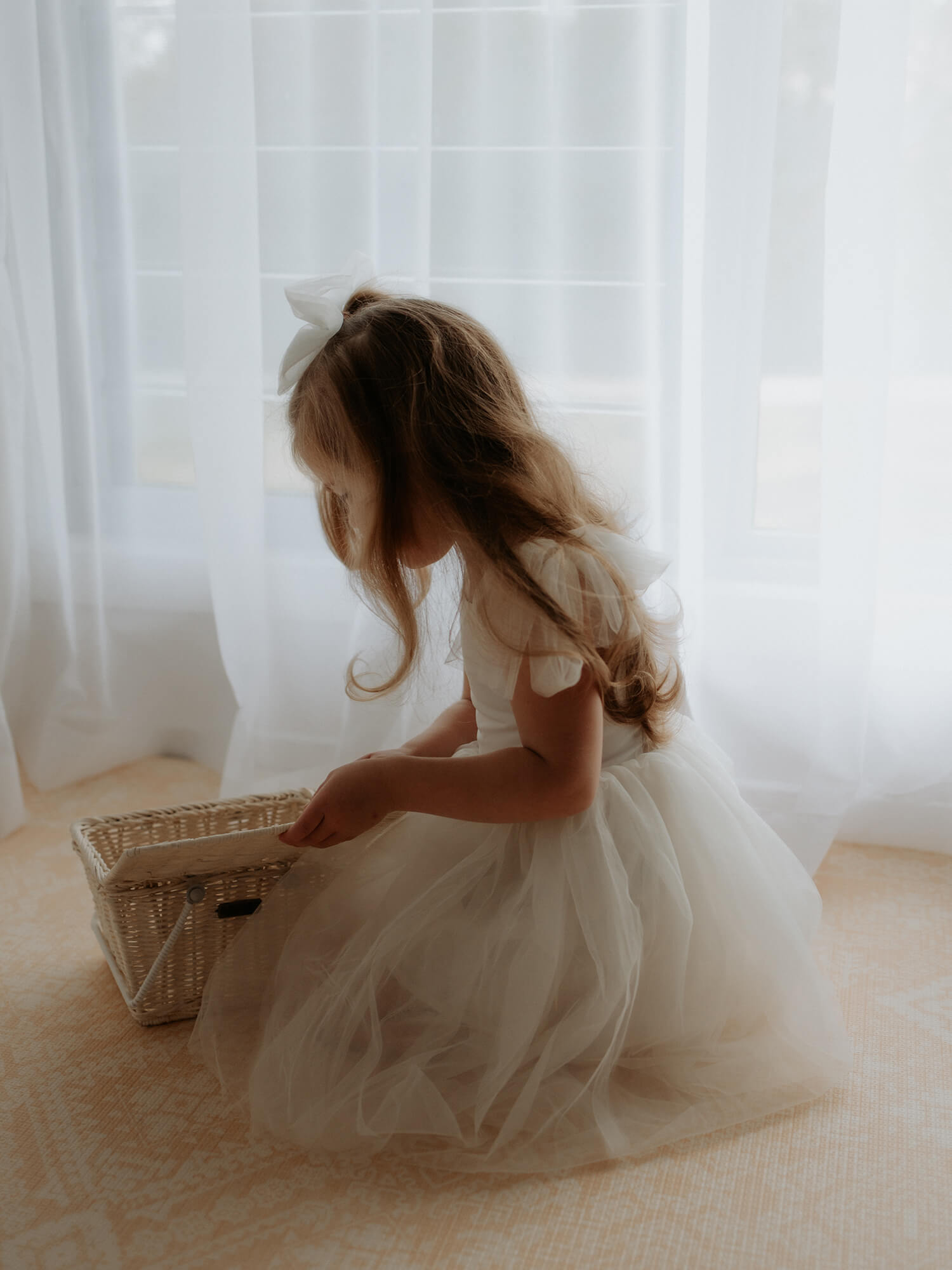 Harper cream flower girl dress is worn by a girl who sits, looking into a basket.