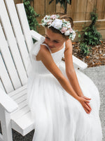 Girl sitting in our Harper white tulle flower girl dress and Daisy floral crown.