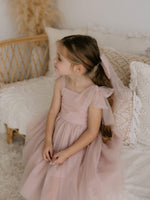 Harper tea length flower girl dress with tulle bow straps is worn by a little girl. She also wears our large dusty pink tulle bow in her hair.