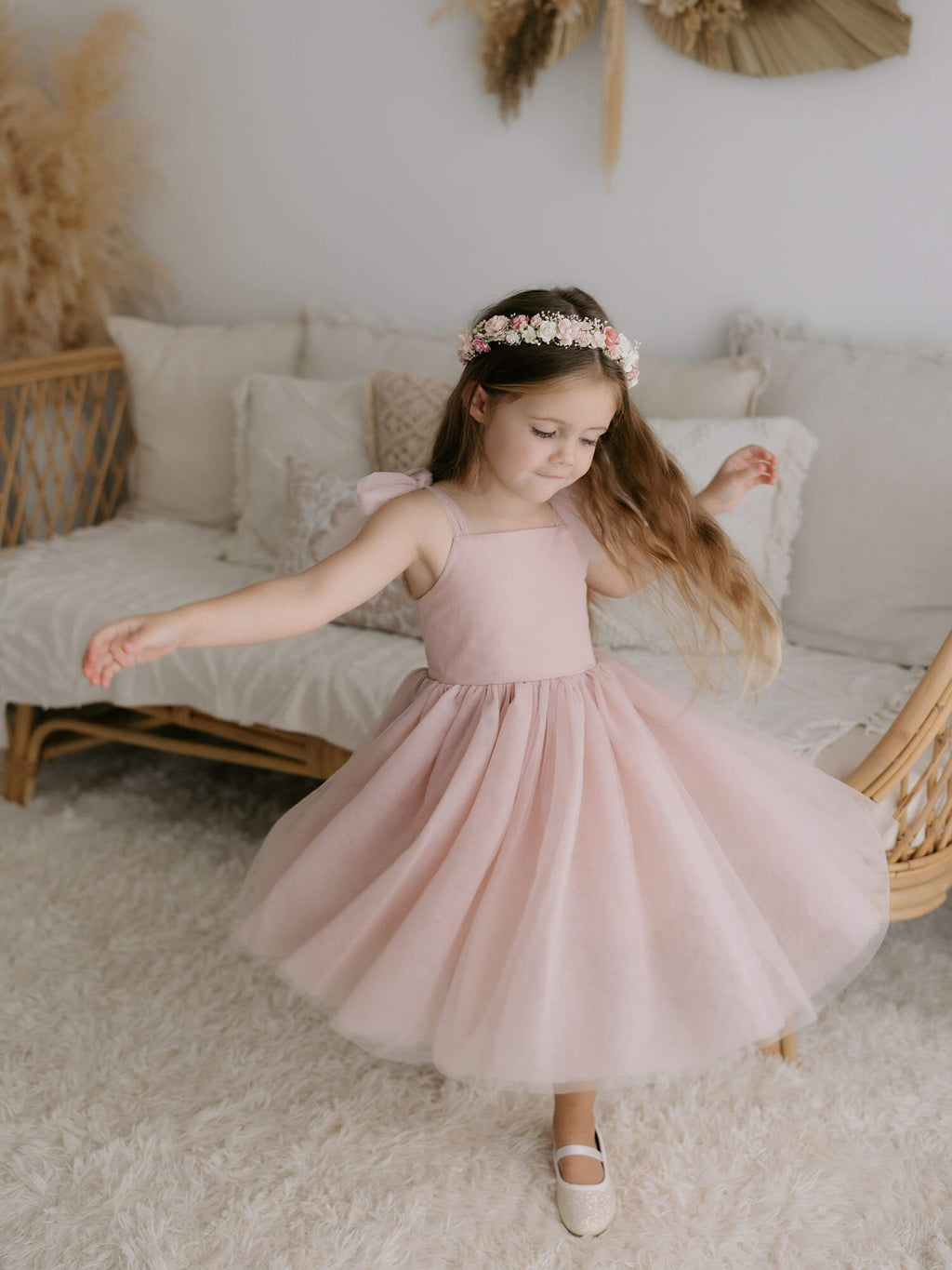 Harper dusty pink tea length flower girl dress, is worn by a young girl who is twirling. She also wears a flower crown in her hair.