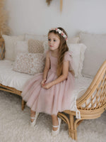 A little girl sits wearing our dusty pink Harper tea length dress and Elsie dusty rose flower crown.