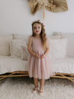 Harper dusty pink flower girl dress is worn by a young girl, with a tea length soft tulle skirt and tulle tie straps.