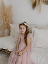 A young girl sits wearing our Harper tea length flower girl dress in dusty pink. She also wears our Elsie dusty rose girls flower crown.