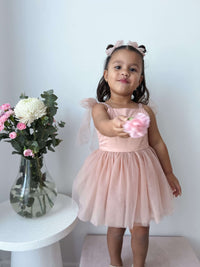 A young girl holds a flower, she wears our Isla baby flower girl dress in champagne and matching tulle bows.