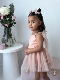 A toddler wears our champagne Isla baby flower girl dress romper and champagne tulle pigtail bow clips.