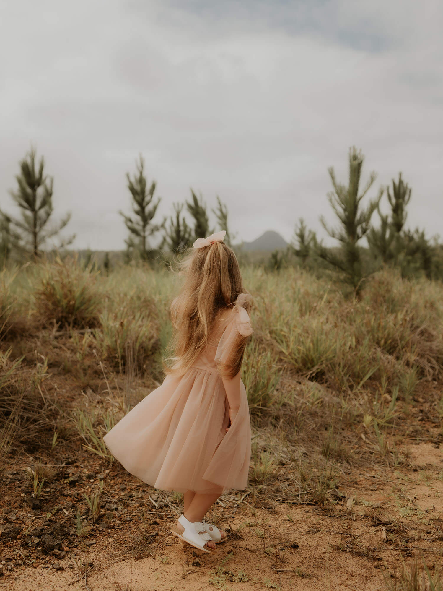 A young girl spins wearing a tulle bow hair clip in champagne and Isla flower girl dress, also in champagne.