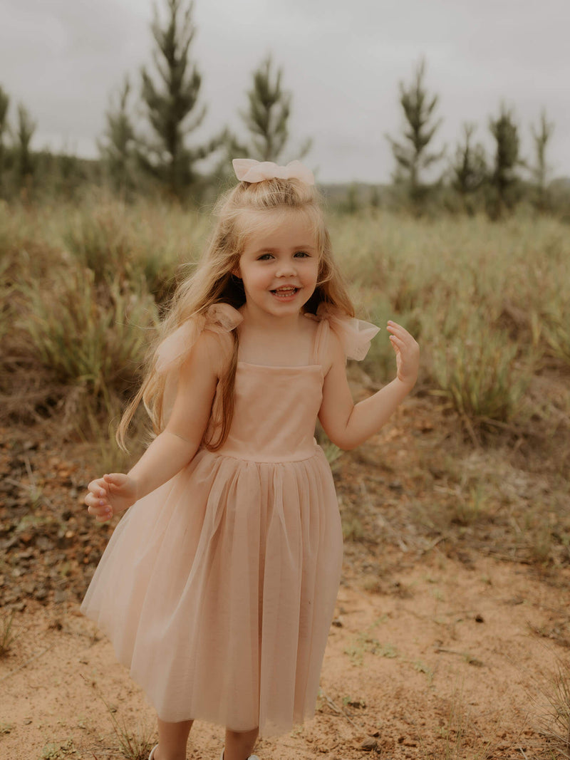 Smiling young girl wears our champagne flower girl dress with soft champagne tulle, Isla dress.