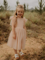 Young girl laughs wearing our Isla flower girl dress in champagne, and tulle bow hairclip in champagne.