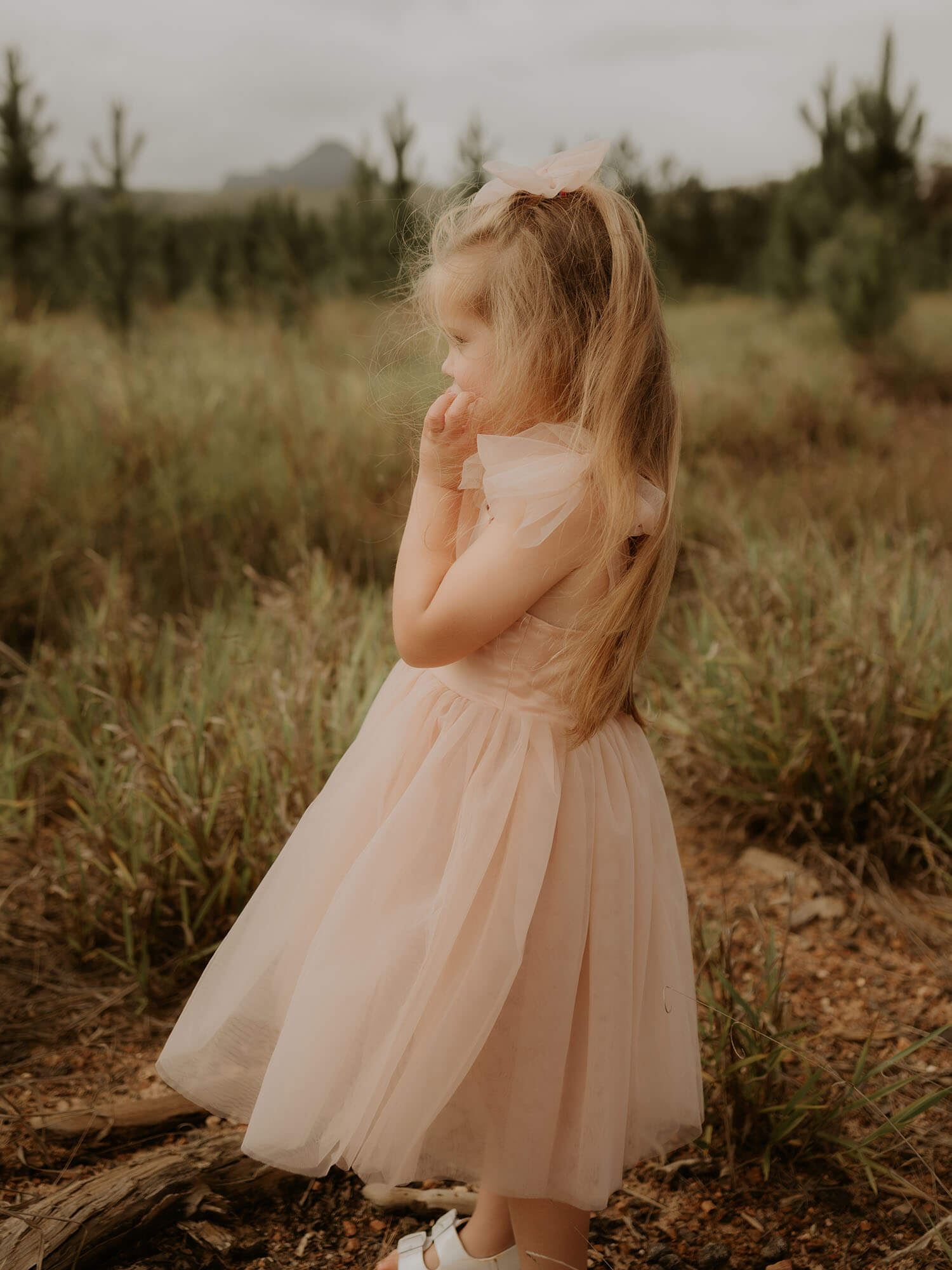 Our Isla champagne flower girl dress with tulle tie sleeves, in colour champagne, is worn with a matching tulle bow hairclip.