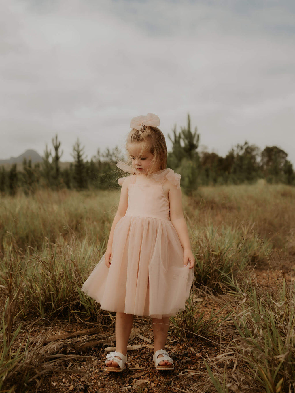Isla champagne flower girl dress is worn by a young girl. She also wears a matching champagne tulle bow in her hair.