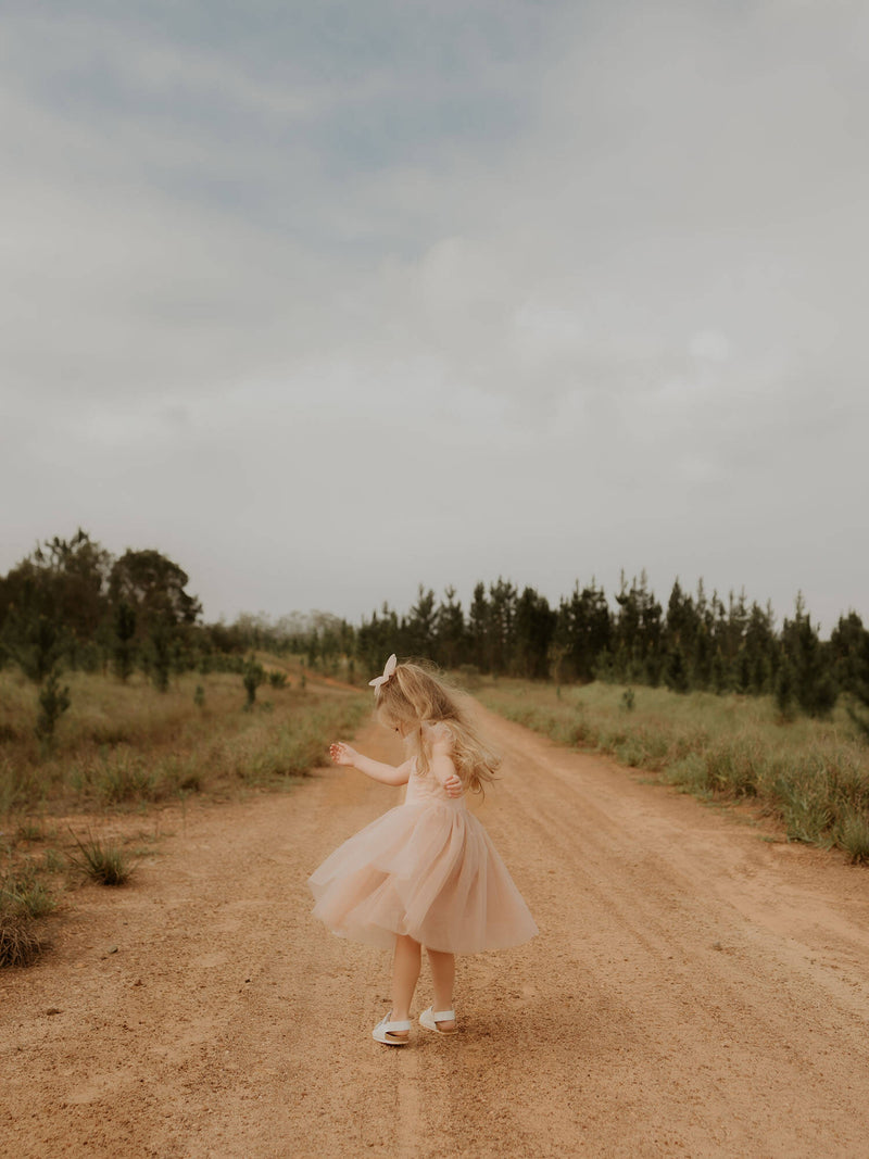 A young girl twirls wearing our Isla flower girl dress in champagne, along with a matching soft tulle hair clip.