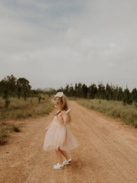 Isla champagne flower girl dress is worn by a young girl, dancing outside.