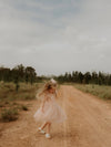 A girl twirling on a dirt road, wearing a soft tulle flower girl dress in champagne, and matching tulle bow hair clip in champagne.