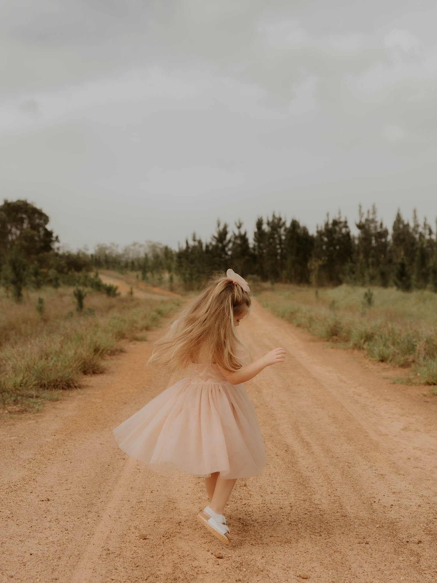 Twirling young girl wears our Isla flower girl dress and girls tulle bow hair clip, both in champagne.