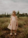 A young girl smiles wearing our champagne tulle bow flower girl dress, and matching tulle bow hair clip.