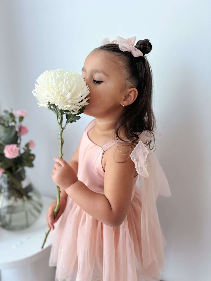 A toddler smells a flower, wearing our champagne Isla toddler flower girl romper.