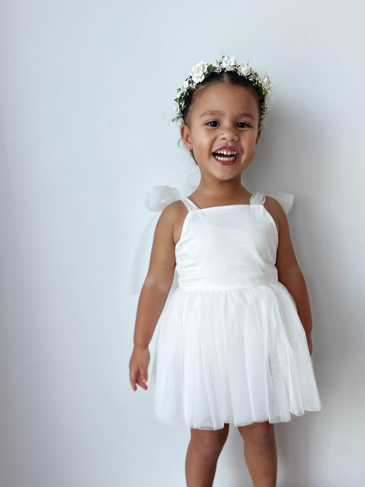 Isla ivory toddler flower girl romper is worn by a young girl. She also wears an ivory flower crown.