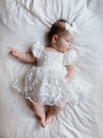 Baby girl is laying down wearing our Kenzi puff sleeve baby flower girl romper and tulle bow headband.