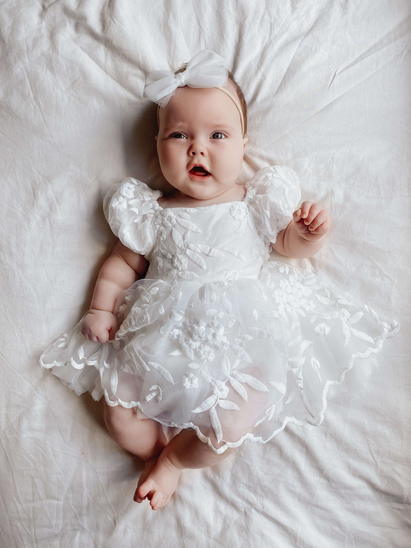 Baby flower girl wears our Kenzi baby dress in ivory and tulle bow headband.