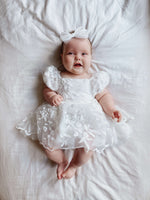 Baby girl smiles wearing our Kenzi baby flower girl dress and tulle bow headband in ivory.