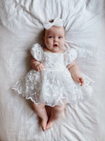 Baby girl wears our Kenzi baby flower girl romper, with embroidered lace tulle. She also wears a tulle bow headband.