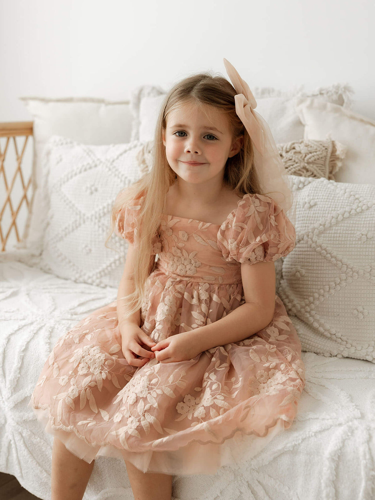 A little girl sits wearing a pink toned flower girl dress, our Kenzi dress in dusty rose.