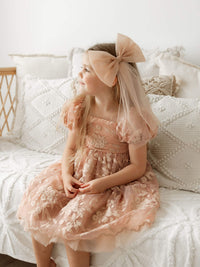 A young girl sits wearing our Kenzi dusty rose flower girl dress with embroidered tulle lace.