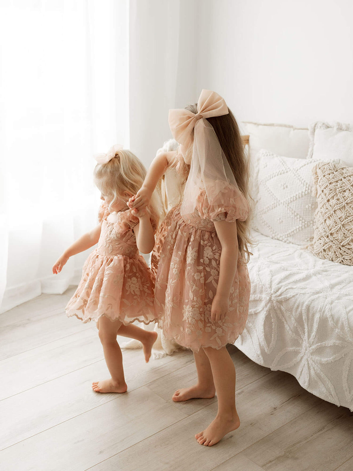 Kenzi puff sleeve dusty rose flower girl dress and baby flower girl romper are worn by two sisters.