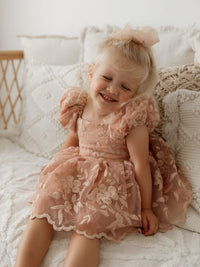 A little girl smiles wearing our dusty rose Kenzi baby flower girl romper.