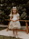 Kenzi ivory lace flower girl dress is worn by a young girl. she also wears an ivory tulle bow in her hair.