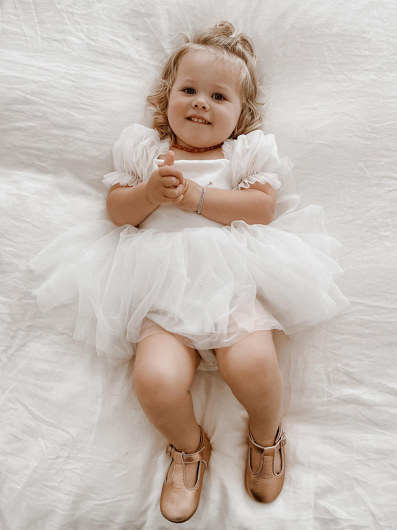 A toddler girl wears our Layla flower girl romper dress in ivory.