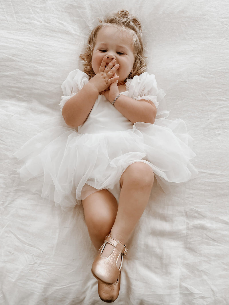 Toddler giggling wearing our Layla tulle puff sleeve baby flower girl romper in ivory.