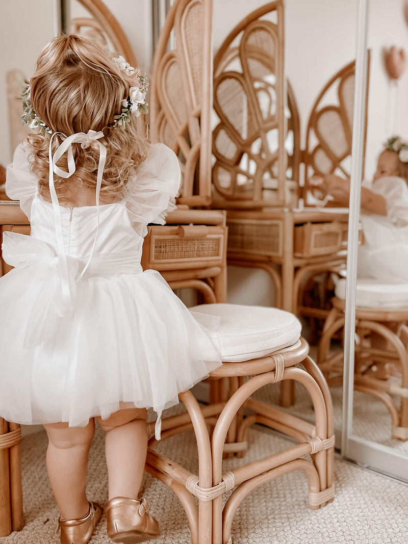 Baby flower girl romper shown from the back, worn by a young toddler. She also wears our Daisy flower crown.