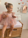 Layla dusty pink baby flower girl dress is worn by a toddler. She also wears matching tulle pigtail bows in her hair.