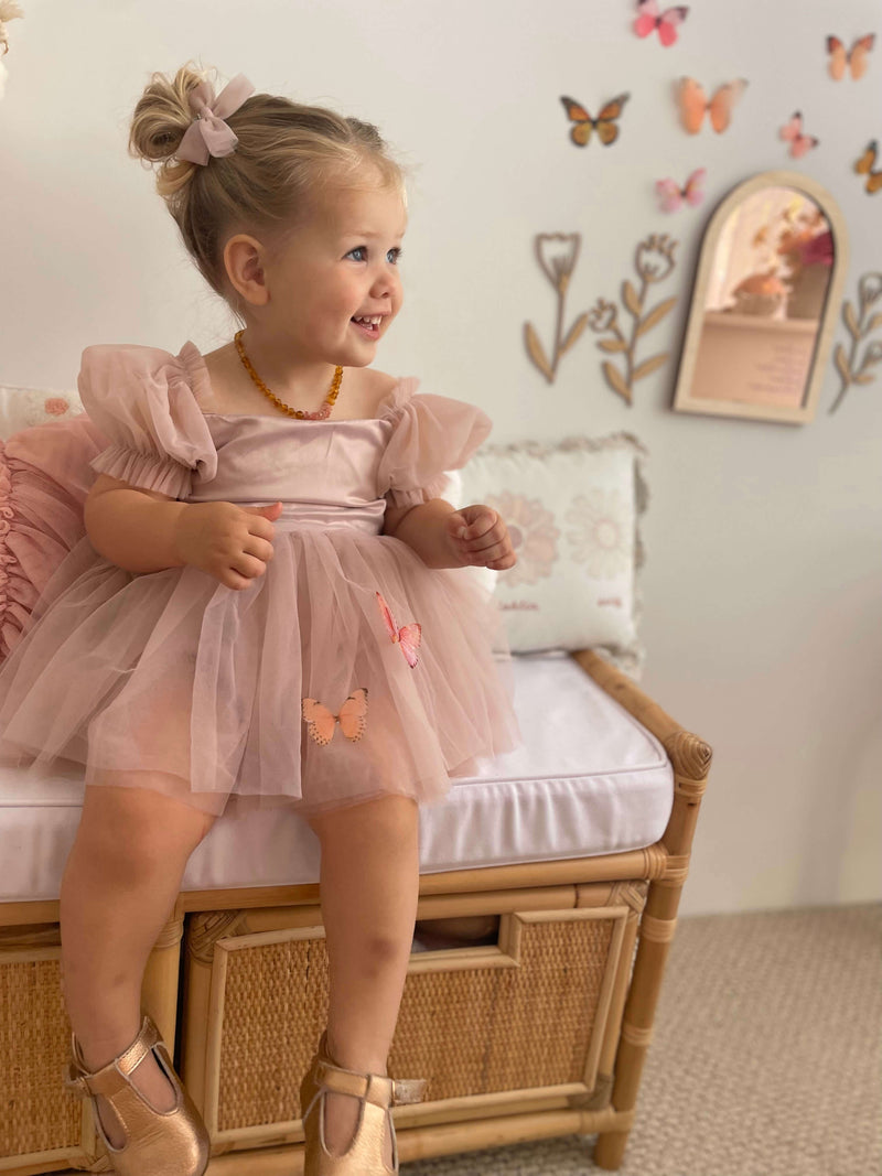 A smiling toddler wears our Layla baby flower girl romper in dusty pink.