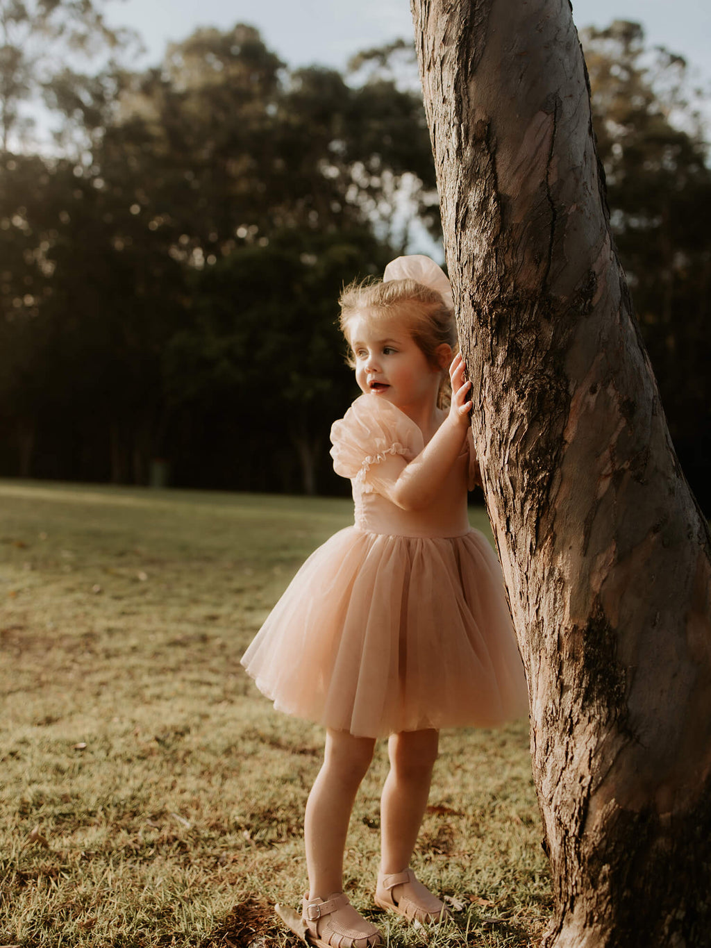 Layla champagne flower girl dress with puff sleeves is worn by a young girl, she also wears a matching tulle bow in her hair.