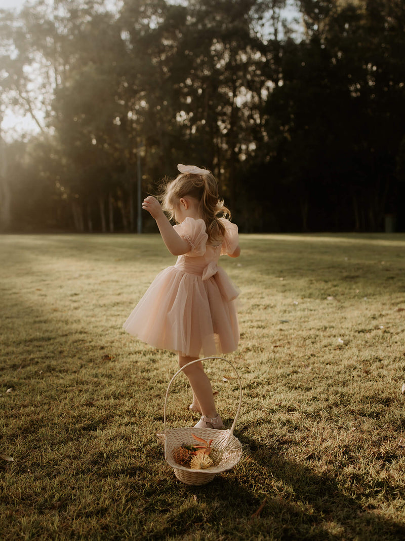 A young girl twirls wearing our Layla champagne flower girl dress, with tulle bow back and tulle puff sleeves.