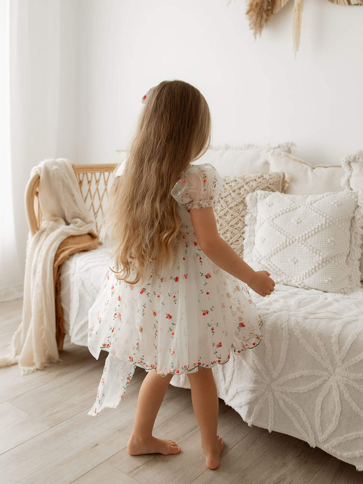 A young girl twirls wearing a red floral Christmas dress with puff sleeves and a bow at the back.