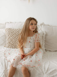 Layla girls Christmas and flower girl dress is worn by a young girl sitting on a couch.