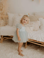 Layla dusty blue tulle puff sleeve flower girl romper is worn by a young girl. She also wears a dusty blue tulle bow clip in her hair.
