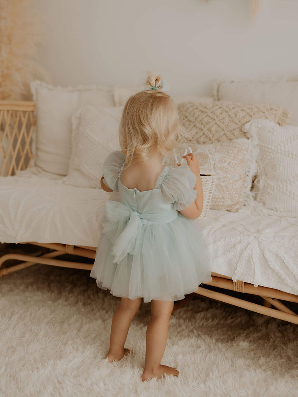 Layla dusty blue baby flower girl dress is worn by a young girl. She also wears a tulle pigtail bow in her hair.