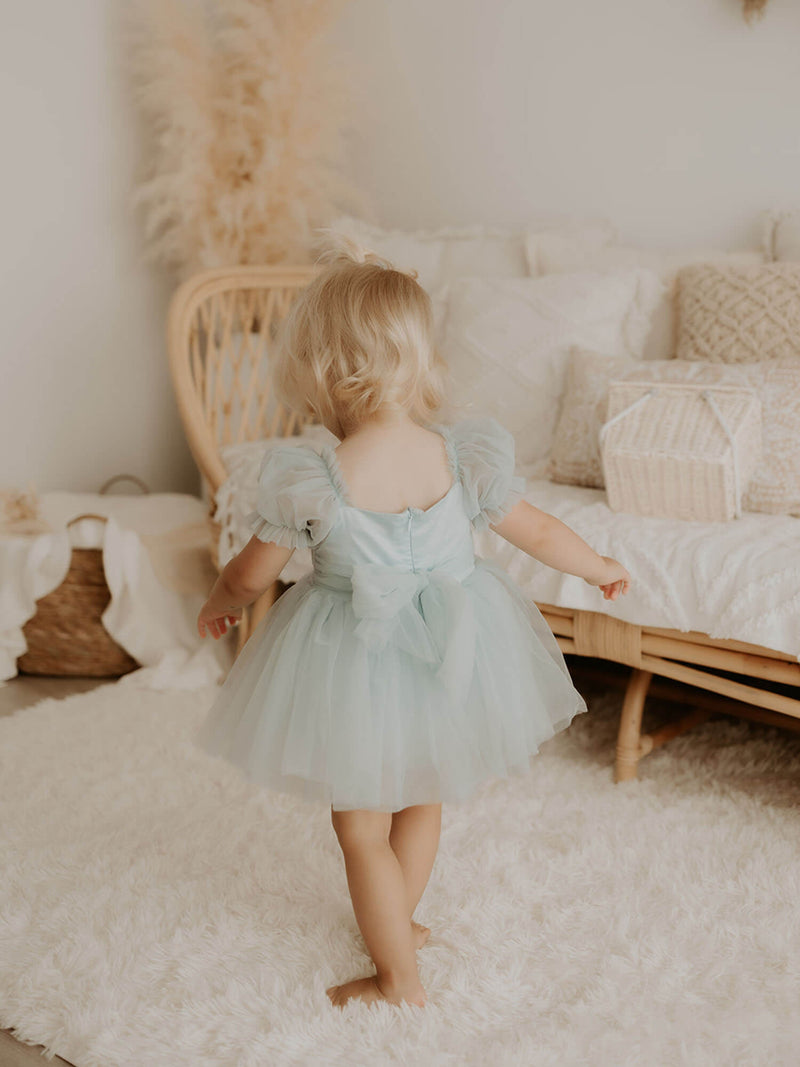 The back of our Layla baby flower girl romper in dusty blue, showing the tulle bow at the back and tulle puff sleeves.