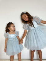 Layla dusty blue flower girl dress is worn by two young sisters. They also wear matching dusty blue tulle bows in their hair.