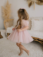 A young girl wears our Layla dusty pink tulle puff sleeve flower girl dress, and a matching tulle bow in her hair.