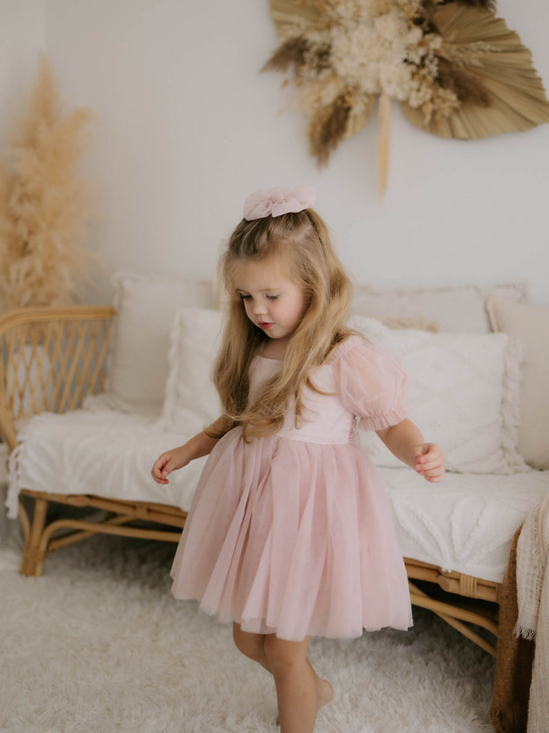 Layla flower girl dress and tulle bow in dusty pink are worn by a young girl.