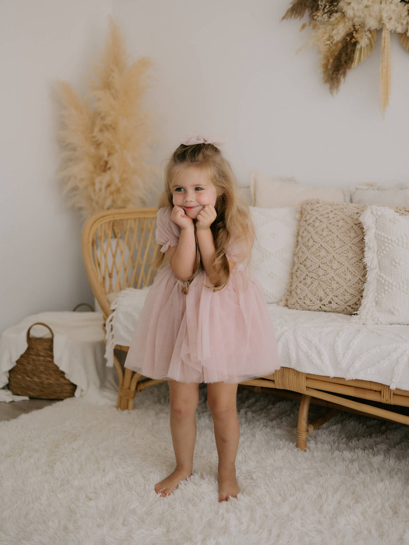 A young girl wears our Layla flower girl dress in dusty pink, and matching tulle bow in her hair.