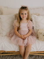 Layla flower girl dress in dusty pink is worn by a young girl. She also wears a dusty pink tulle bow in her hair.