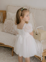 Our Layla flower girl dress in ivory is worn by a young girl. It has tulle puff sleeves and a tulle bow at the back.