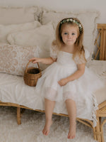 Layla flower girl dress is worn by a young girl sitting on a couch.