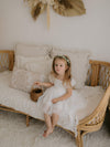 A young girl sits on a seat, holding a basket and wearing our Layla flower girl dress with tulle puff sleeves.